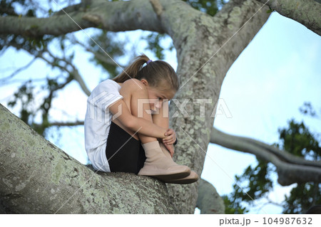 Young pretty child girl sitting relaxed between big branches of old tree on sunny summer day 104987632