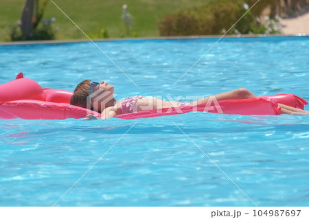 Young child girl relaxing on summer sun swimming on inflatable air mattress in swimming pool during tropical vacations. Summertime activities concept 104987697