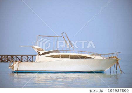 White motor boat floats in ocean water at long pier bridge under bright blue sky, view from sandy beach. Summer traveling concept White motor boat floats in ocean water at long pier bridge under bright blue sky, view from sandy beach. Summer traveling concept 104987800