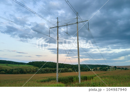 Tower with electric power lines for transfering high voltage electricity located in agricultural cornfield. Delivery of electrical energy concept. Tower with electric power lines for transfering high voltage electricity located in agricultural cornfield. Delivery of electrical energy concept. 104987940