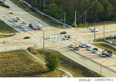 Top view of wide road with moving cars at intersection with traffic lights. City transportation in the USA. American town traffic from above Top view of wide road with moving cars at intersection with traffic lights. City transportation in the USA. American town traffic from above 104987951