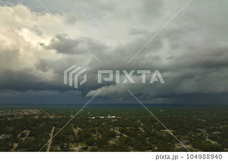 Dark stormy clouds forming on gloomy sky before heavy rainfall over suburban town area 104988940