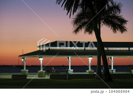 Dark silhouette of people resting under alcove roof on sea shore in public park at sunset 104988984