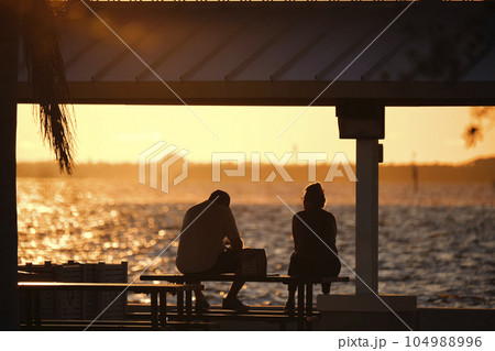 Dark silhouette of people resting under alcove roof on sea shore in public park at sunset 104988996