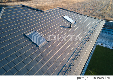 Closeup of attic windows on house roof top covered with ceramic shingles. Tiled covering of building 104989176