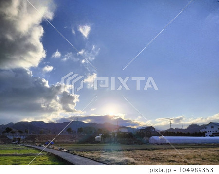 夕刻の空に落ちていく光る太陽と田舎の田んぼの風景 104989353