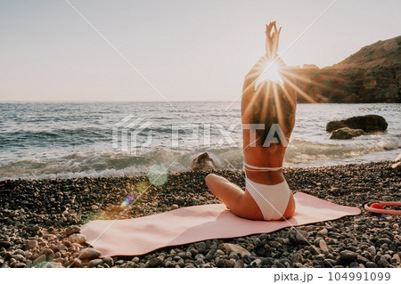 Woman sea yoga. Happy woman in white swimsuit and boho style braclets practicing outdoors on yoga mat by sea on sunset. Women yoga fitness routine. Healthy lifestyle, harmony and meditation Woman sea yoga. Happy woman in white swimsuit and boho style braclets practicing outdoors on yoga mat by sea on sunset. Women yoga fitness routine. Healthy lifestyle, harmony and meditation 104991099
