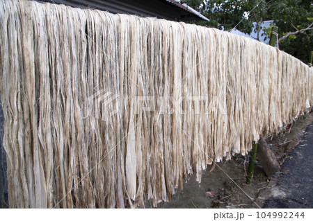 Close-up shot of raw jute fiber hanging under the sunlight for drying. Brown jute fiber texture 104992244