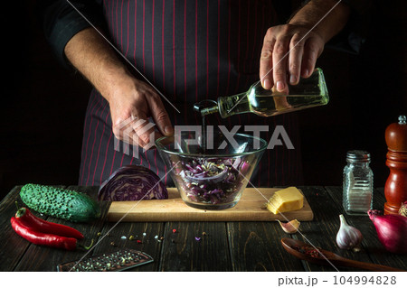 The cook adds oil to the red cabbage salad. Cooking a delicious vegan dish with the hands of a chef in the kitchen. Menu idea for hotel or restaurant 104994828