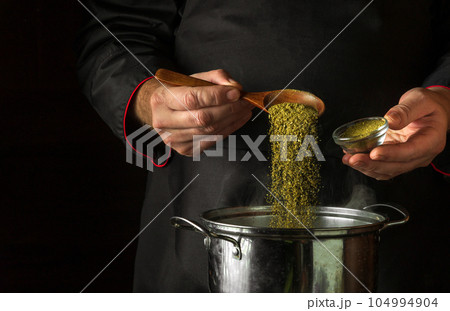 The chef adds dry spices to a pot of boiling food. Retsoran kitchen cooking concept with advertising space on black background The chef adds dry spices to a pot of boiling food. Retsoran kitchen cooking concept with advertising space on black background 104994904