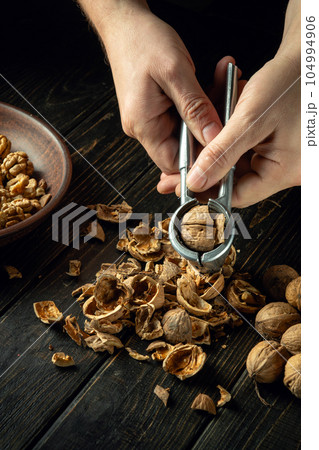 The cook is peeling walnuts on the kitchen table. Close-up of the chef hands while working. Culinary concept on dark background The cook is peeling walnuts on the kitchen table. Close-up of the chef hands while working. Culinary concept on dark background 104994906