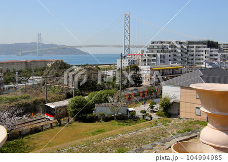 明石海峡大橋を五色塚古墳から山陽電鉄霞ヶ丘駅東側の山陽電鉄6000系越しに望む 104994985