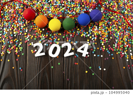 White numbers 2024 and color sugar sprinkles on wooden table with color balls garland 104995040