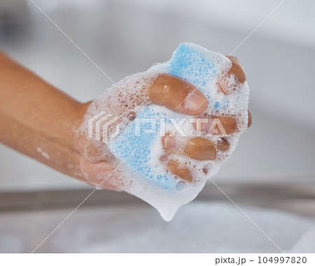 Time to tackle the dirty dishes. Closeup shot of an unrecognisable woman squeezing soap from a sponge at home. Time to tackle the dirty dishes. Closeup shot of an unrecognisable woman squeezing soap from a sponge at home. 104997820