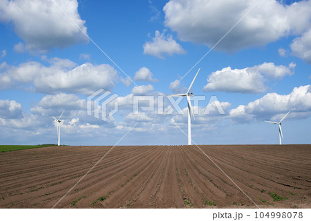Wind turbines and environmental infrastructure isolated against blue sky with copy space on an empty energy farm. Propellers converting sustainable energy into electric power in remote and rural area Wind turbines and environmental infrastructure isolated against blue sky with copy space on an empty energy farm. Propellers converting sustainable energy into electric power in remote and rural area 104998078