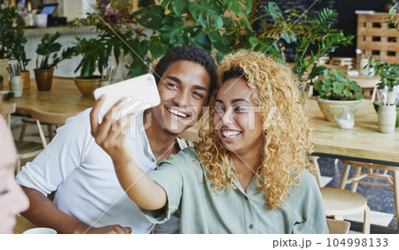 Making memories to last a lifetime. Shot of a young couple taking selfies in a coffee shop using a mobile phone. Making memories to last a lifetime. Shot of a young couple taking selfies in a coffee shop using a mobile phone. 104998133