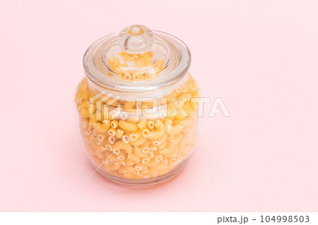 Uncooked Chifferi Rigati Pasta in Glass Jar on Pink Background Uncooked Chifferi Rigati Pasta in Glass Jar on Pink Background 104998503