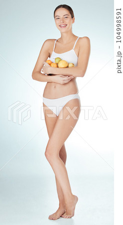 Eat right, feel light. Studio shot of an attractive and fit young woman holding fruit against a blue background. Eat right, feel light. Studio shot of an attractive and fit young woman holding fruit against a blue background. 104998591