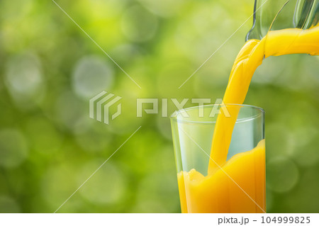 orange juice pouring into glass from jug on green background 104999825