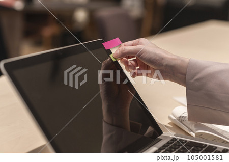 ノートパソコンに付箋を貼る女性の手 105001581