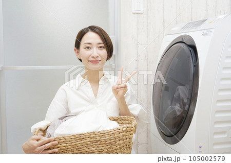 洗濯機の前で洗濯物を持ってピースサインするミドルエイジの女性 105002579