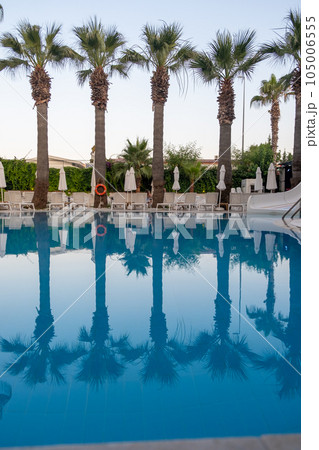 Luxurious hotel with swimming pool, palm trees, sun loungers and seating area. Palm trees are reflected in the clear water of the pool. Luxurious hotel with swimming pool, palm trees, sun loungers and seating area. Palm trees are reflected in the clear water of the pool. 105006555