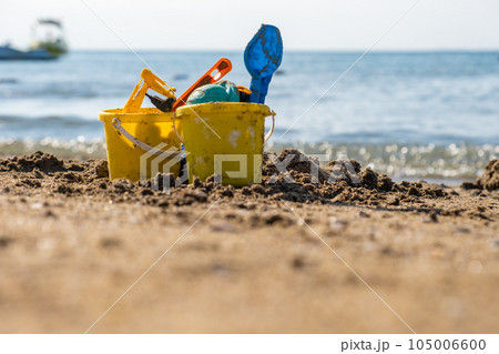 Children's beach toys - buckets, spade and shovel on sand on a sunny day. Bright toys on the background of the sea. 105006600