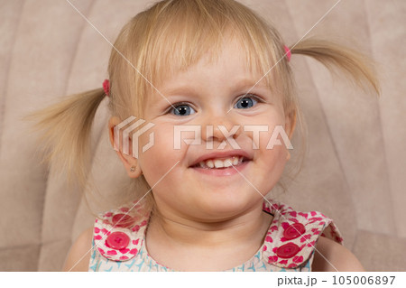Portrait of a 2-year-old blonde girl with blue eyes who looks at the camera smiling 105006897