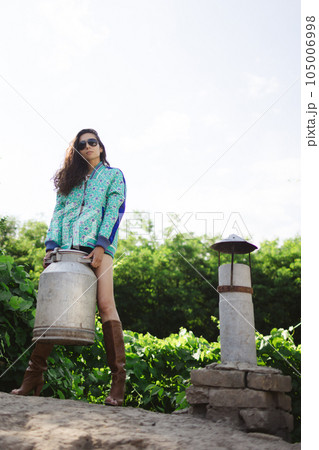 Young fashionable farmer woman posing on camera while holding milk can. Young fashionable farmer woman posing on camera while holding milk can. 105006998