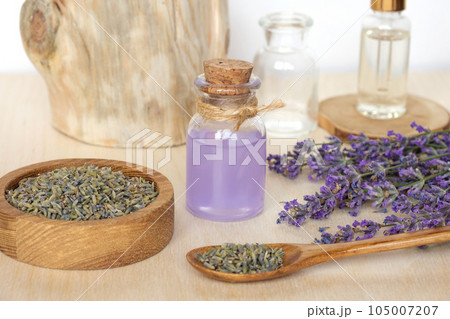 Dry lavender flowers in wooden bowl and bottle of essential lavender oil or infused water on white background. Natural organic ingredients for herbal cosmetics. Spa massage set, lavender product Dry lavender flowers in wooden bowl and bottle of essential lavender oil or infused water on white background. Natural organic ingredients for herbal cosmetics. Spa massage set, lavender product 105007207