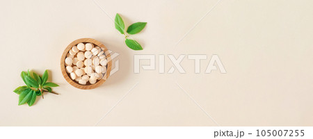 Directly Above Shot Of Pills and green leaves. Tablets in wooden bowl on beige neutral colors background. Homeopathic medicine. Organic medical capsules with herbal plant. Table top view. Copy space Directly Above Shot Of Pills and green leaves. Tablets in wooden bowl on beige neutral colors background. Homeopathic medicine. Organic medical capsules with herbal plant. Table top view. Copy space 105007255
