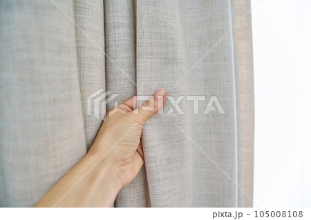 Light beige sand linen natural curtains on window, close-up of hand touching curtains 105008108