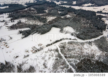 Aerial view of barren winter landscape with mountain hills covered with evergreen pine forest after heavy snowfall on cold quiet evening. Aerial view of barren winter landscape with mountain hills covered with evergreen pine forest after heavy snowfall on cold quiet evening. 105008389