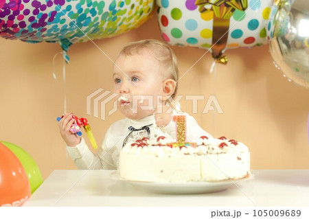A child with a smeared face in a cake near a burning candle 1 year old. A child with a smeared face in a cake near a burning candle 1 year old. 105009689