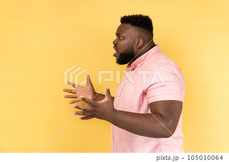 Side view of annoyed stressed man wearing pink shirt asking what do you want and spreading hands, family quarrel, misunderstanding. Indoor studio shot isolated on yellow background. 105010064