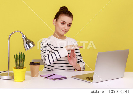 Tired woman manager showing time out gesture looking at laptop screen, talking on video call, asking pause, break of online communication. Indoor studio studio shot isolated on yellow background. 105010341
