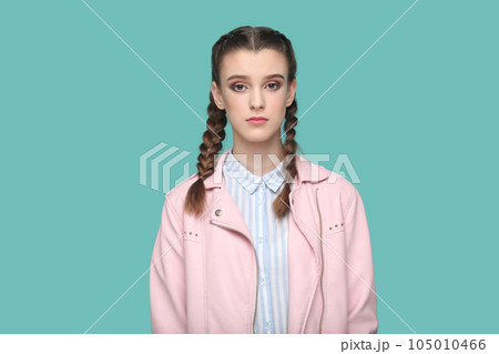 Portrait of serious strict young teenager girl with braids wearing pink jacket looking at camera with bossy expression, being in bad mood. Indoor studio shot isolated on green background. Portrait of serious strict young teenager girl with braids wearing pink jacket looking at camera with bossy expression, being in bad mood. Indoor studio shot isolated on green background. 105010466