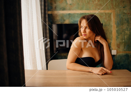Portrait of a beautiful and sexy young woman in a black bustier at a table. Portrait of a beautiful and sexy young woman in a black bustier at a table. 105010527