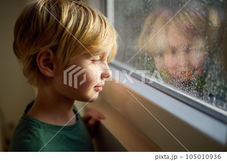 Portrait of preteen boy standing at the window. Child watching the rain outside. 105010936