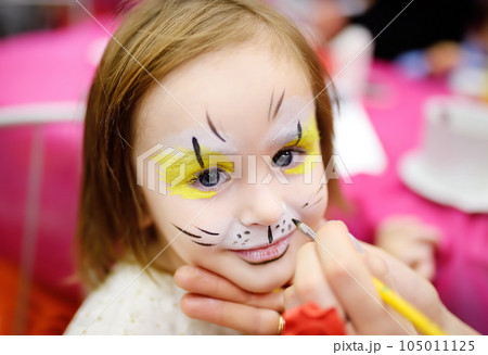 Face painting for cute little gorl during kids merriment. Face paint for "Animals" theme on birthday party. Preschooler kids celebrating party in entertainment center. 105011125