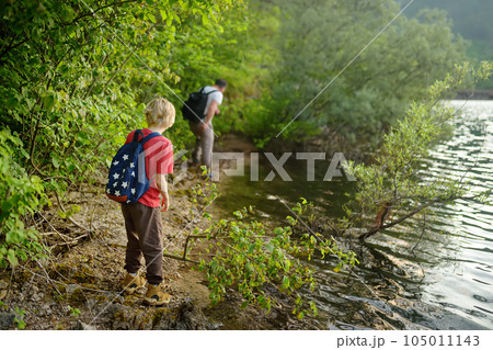 School child boy and father are hiking along forest lake and exploring nature. Family traveling in woodland. Summer vacation activity for inquisitive kids. Adventure, scouting, tourism for children 105011143