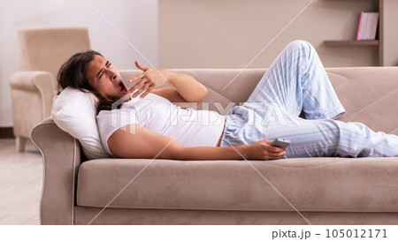 Young lazy man in oversleeping concept at home 105012171