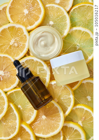 Top view of an amber dropper bottle, yellow cream jar places on surface of orange slices. Mockup scene for advertising cosmetic with lemon extract. Beauty herbal skincare product concept. 105016217
