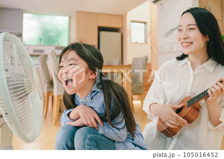 扇風機に向かって大声で歌う女の子とウクレレを弾く母親 105016452