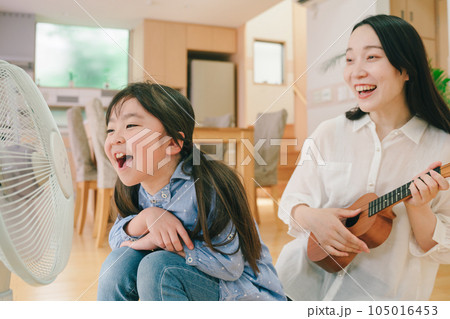 扇風機に向かって大声で歌う女の子とウクレレを弾く母親 105016453