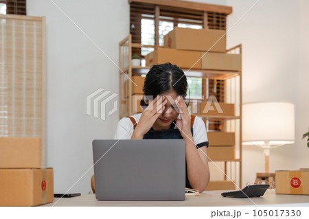 Small online business owner Asian woman wearing apron stressed headache taking Less sales, returned products at home 105017330