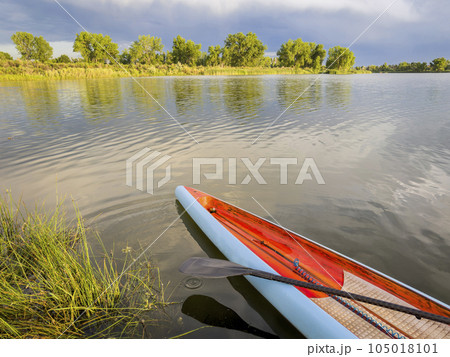 carbon fiber paddle on a deck of racing stand up paddleboard, calm lake with stormy clouds in Colorado carbon fiber paddle on a deck of racing stand up paddleboard, calm lake with stormy clouds in Colorado 105018101