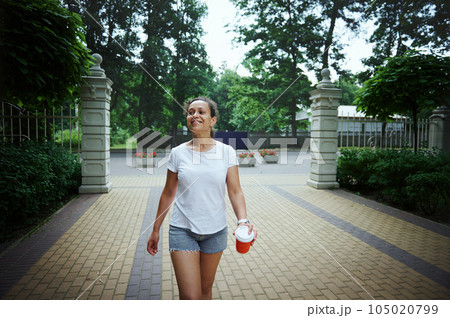 Happy young confident multi-ethnic woman strolling the street. Female walking in the park on a beautiful warm summer day 105020799