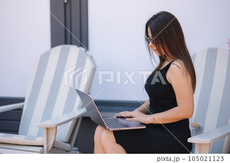 Side view of beautiful woman working outdoors on chair. Female using laptop  105021123