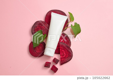Concept for advertising organic cosmetic with natural extract. White plastic tube decorated with beetroot slices and fish mint leaves on a pink background. Top view, blank space for design 105022662
